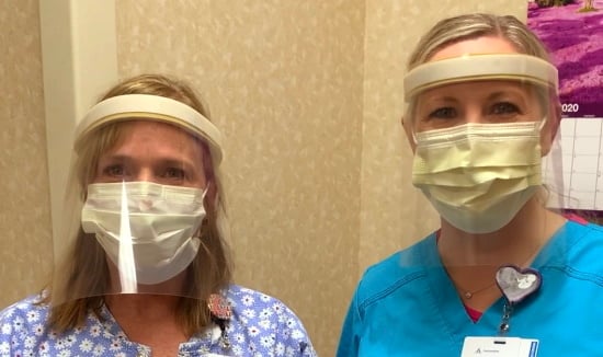 Two women in scrubs wearing surgical masks and plastic face shields.