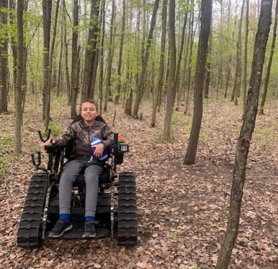 A boy rides an Action Trackchair in the woods.