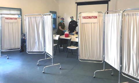 A room set up for vaccinations with two people behind curtained off area wearing PPE.