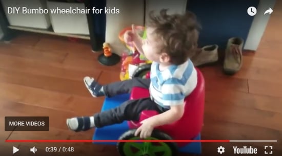 Screenshot of YouTube video titled: DIY Bumbo wheelchair for kids. Shows a toddler giving the thumbs up while seated in his homemade Bumbo wheelchair.