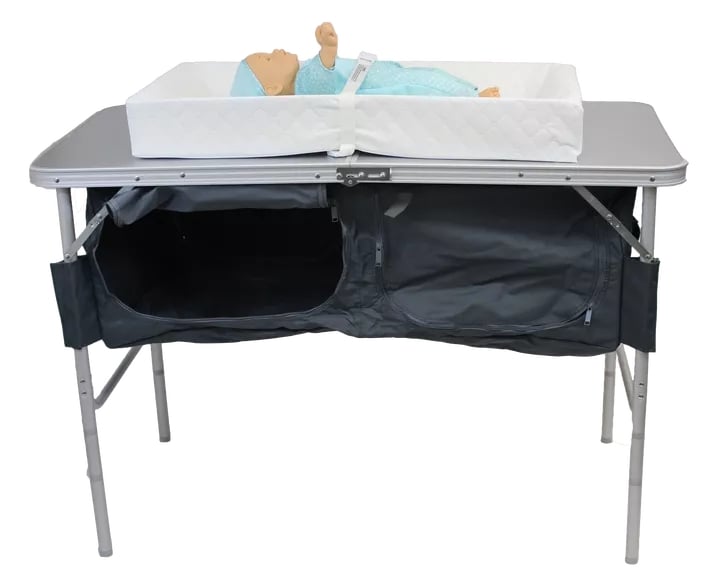 A metal folding table with storage compartments and a changing pad holding a strapped-in doll.