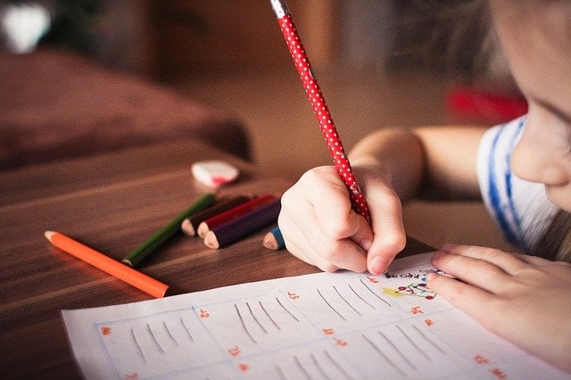 Child writing with colored pencils at desk.
