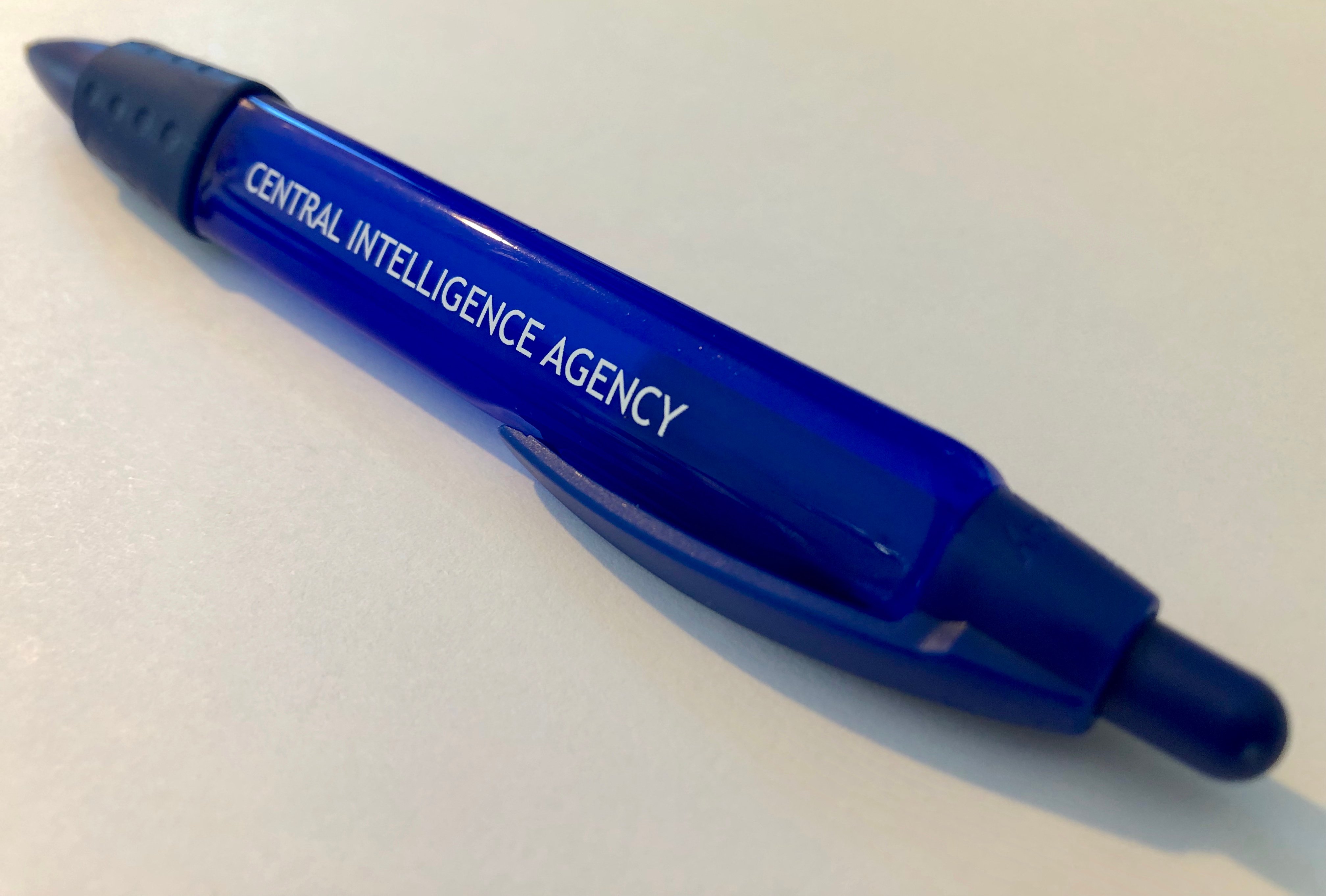 A plastic button-top retractable pen with the words Central Intelligence Agency on one of its three sides. Has rubber grip band and a clip.