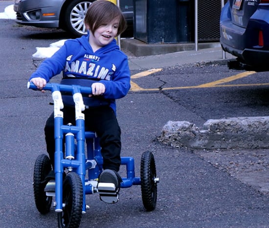 Smiling young boy on a PVC-built trike peddling in a parking lot. 