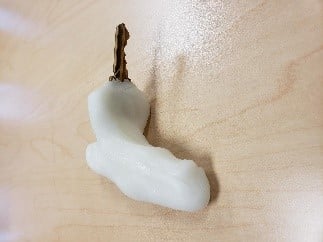 A key encased in white plastic with a handle molded  for a hand grip.