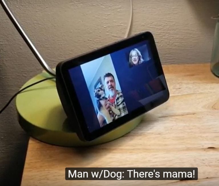 A small monitor on a night stand shows a man holding a puppy on one side and a woman's smiling face in the opposite upper corner. 