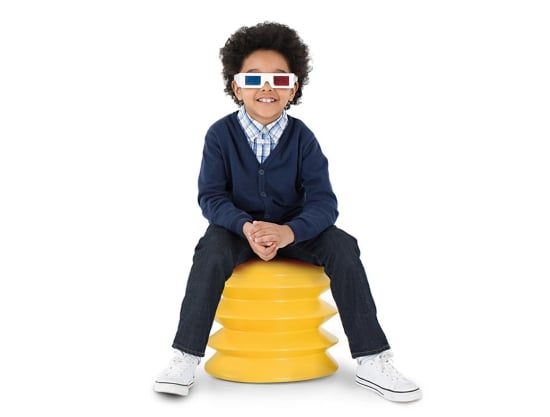 Cute smiling boy wearing 3D paper glasses seated on ergoergo stool which is a plug shape with accordion folds in yellow plastic.