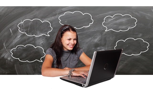 Young woman working on laptop with chalk board behind featuring cloud bubbles.