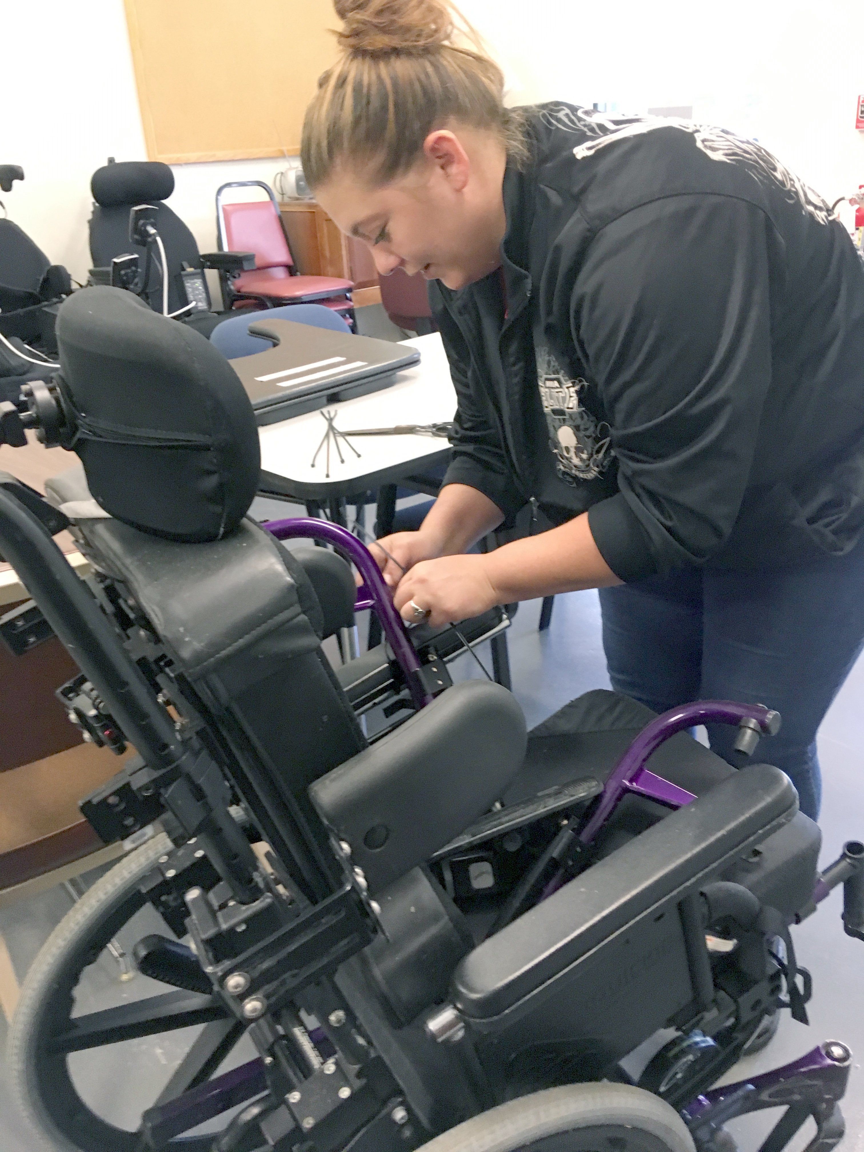 A woman works on a pediatric wheelchair in a room of equipment