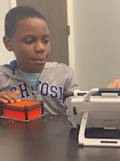 An African-American boy seated at a table using an iPad in a rugged case with a switch.