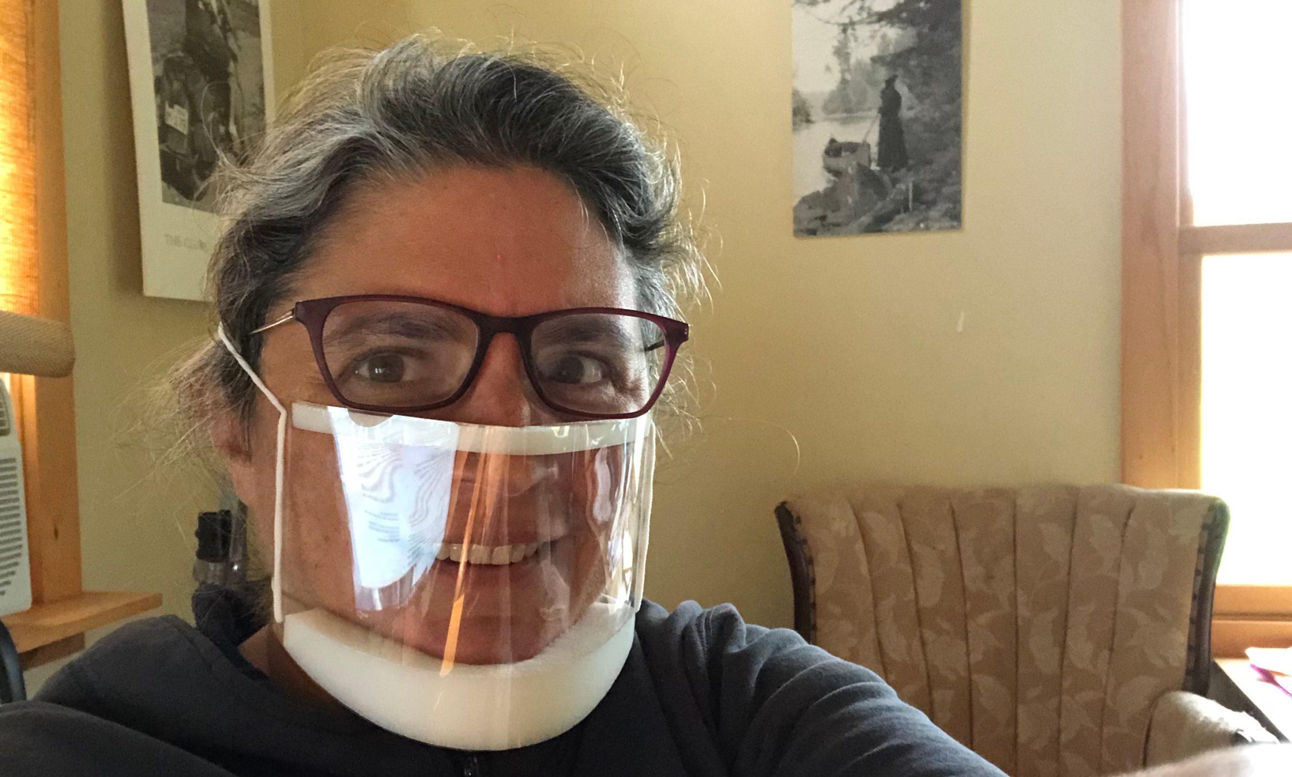 The author smiles wearing a clear mask that is pushing her glasses high on her face and showing considerable glare.