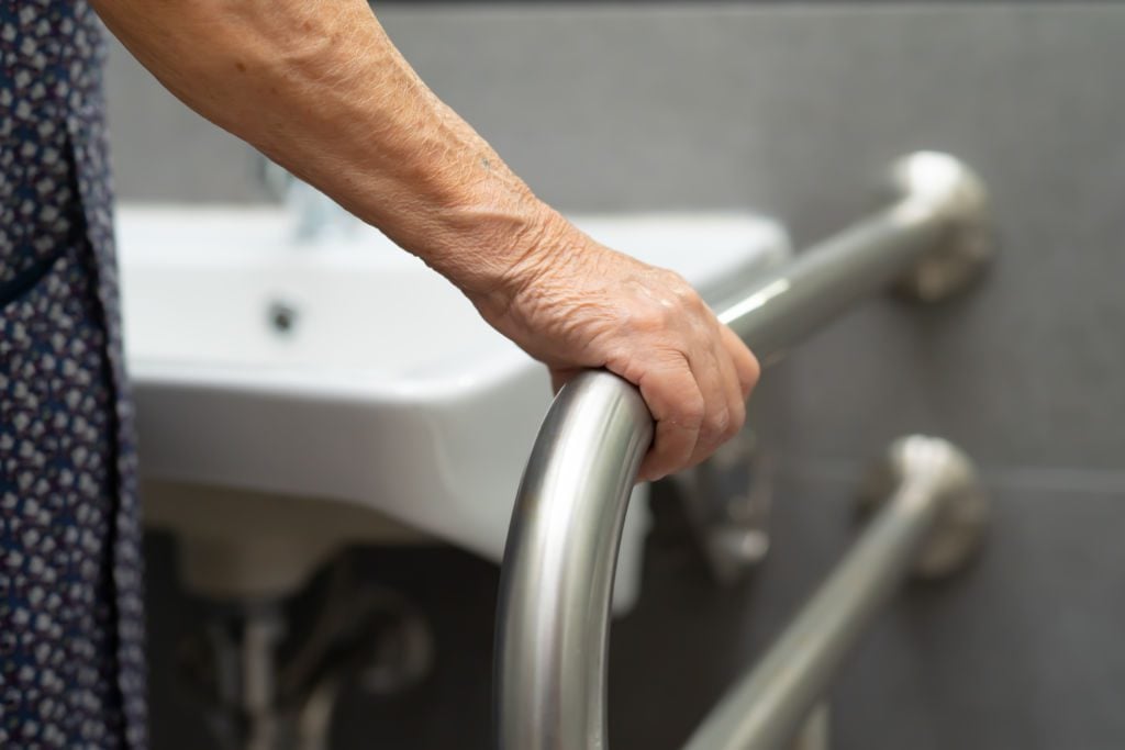 Close up of a hand on a grab bar in a bathroom.