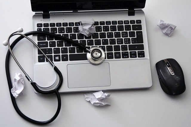 A laptop with a stethoscope and balled up notes.