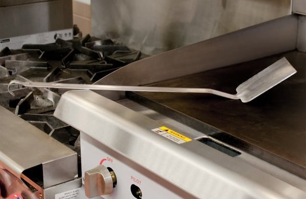 A long metal spatula resting on a gas grill top.