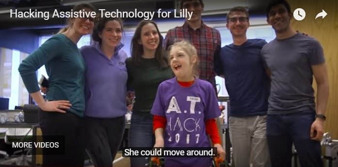 YouTube player screen shot shows young girl wearing AT Hack 2017 t-shirt, standing with walker device, surrounded by smiling college students. Caption says "she could move around." Video title is Hacking Assistive Technology for Lilly.