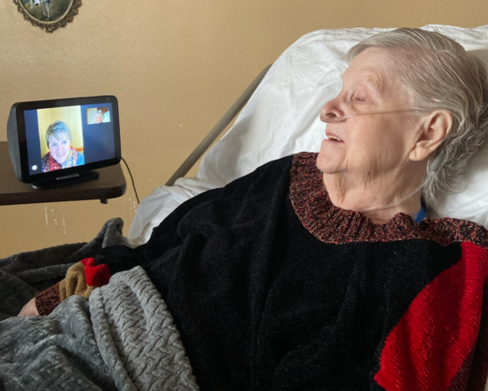 An older woman in bed looks at woman on a screen bedside.