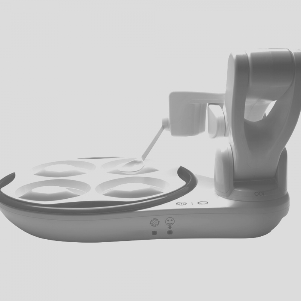 A sleek robotic device featuring four rotating bowls and a spoon mounted to a mechanical arm.