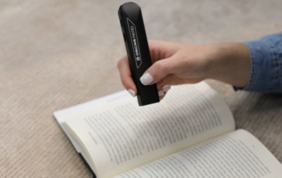 A hand holds a pen-like device above an open book.