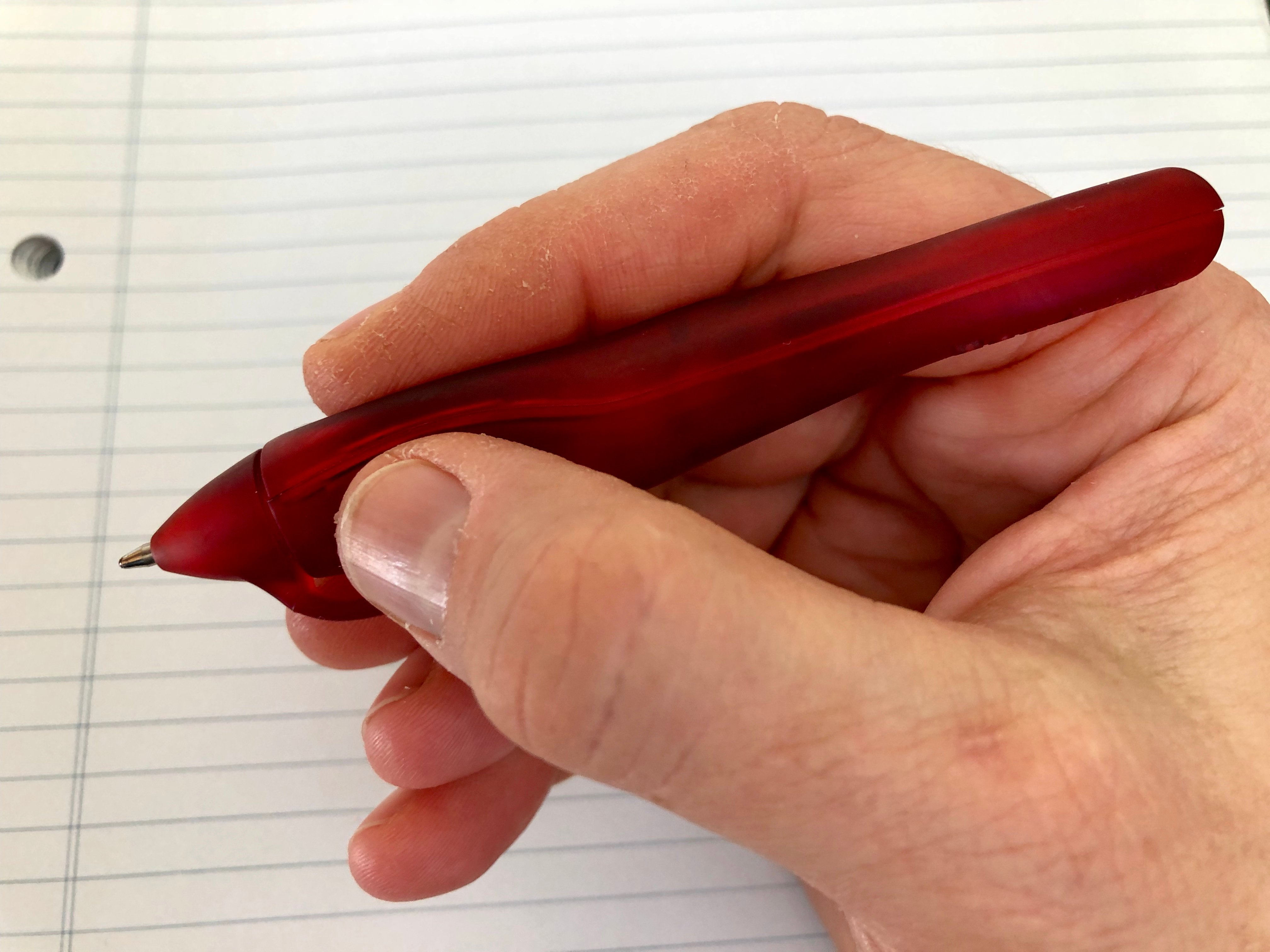 A hand holds the PenAgain pen over lined paper.
