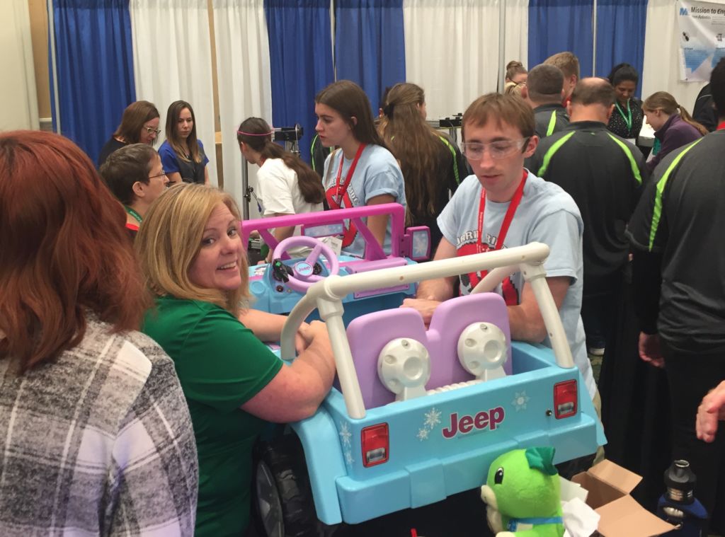 Un jeune homme et une jeune femme travaillent sur un jouet Jeep dans un hall d'exposition très fréquenté.