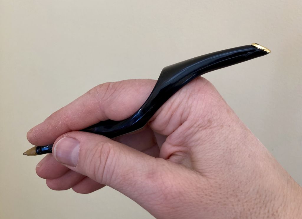A hand holds the RinG-Pen with forefinger inserted through ring. Pen extends in either direction from the base of the forefinger.