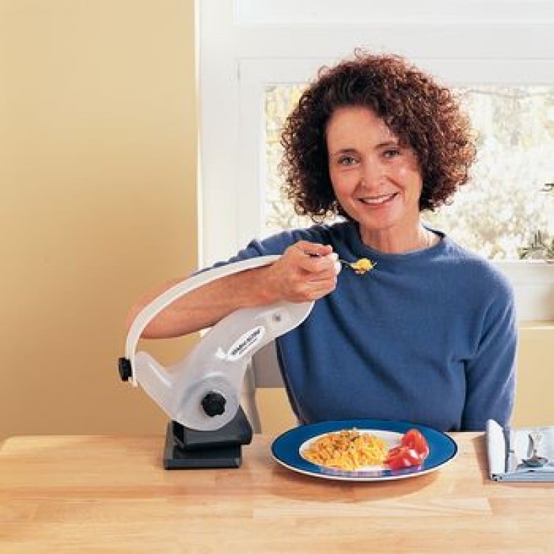 A woman seated eating with a fork with her arm supported in a large mounted loop-shaped bracket device that is hinged and swivels.