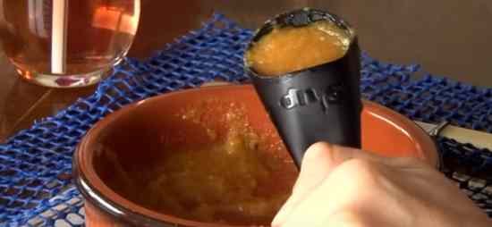 A bowl of thick soup and a plastic spoon shaped like a horn filled with the soup held by a hand. The word S'up is printed on the top of the spoon.