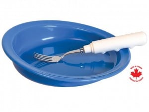 A deep-rimmed plastic plate with one high asymmetrical side. There is an ergonomic fork resting inside.
