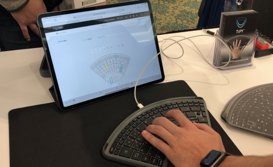 A wedge-shaped one-handed keyboard with a hand typing before a tablet displaying learn software.