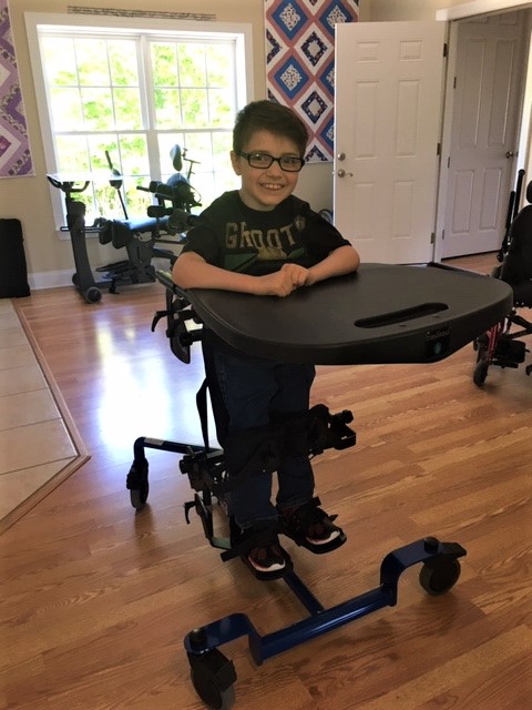 A smiling boy at home in his stander with tray.