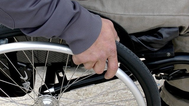 Close-up of a hand grasping the wheel and rim of a wheelchair by the seated chair user.