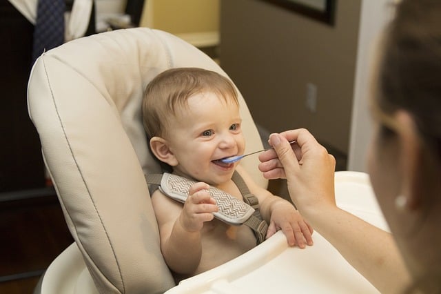 Smiling baby in high chair being fed with a spoon
