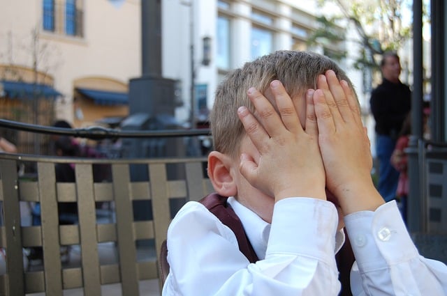 Young boy with hands over face in shame.
